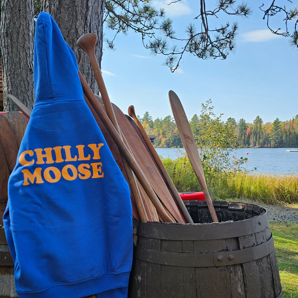 Blue sweatshirt with 'Chilly Moose' text on a wooden surface near a lake.