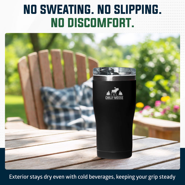 A black insulated tumbler with a clear lid sits on a wooden outdoor table, with a blurred Adirondack chair and greenery in the background. Text at the top reads 'NO SWEATING.#colour_midnight