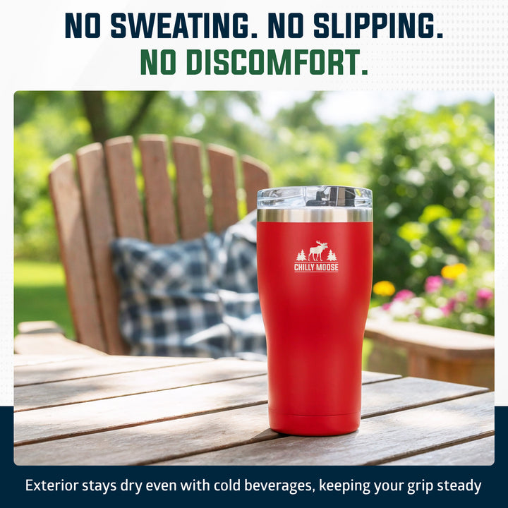 A red insulated tumbler with a clear lid and silver rim sits on a wooden outdoor table, with a blurred Adirondack chair and green garden in the background. Text at the top reads 'NO SWEATING.#colour_canoe-red