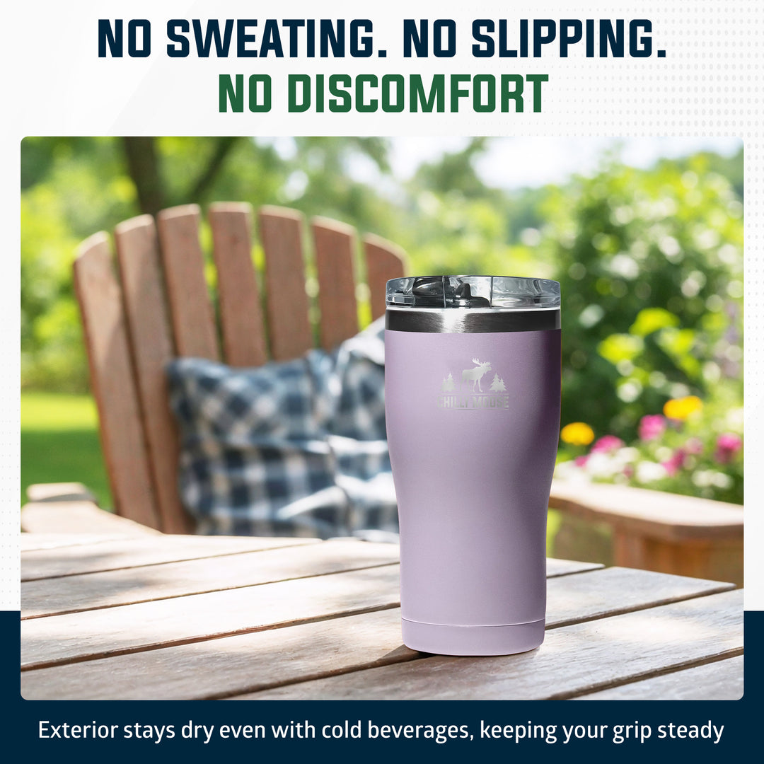 A lavender insulated tumbler with a clear lid sits on a wooden outdoor table, with a blurred Adirondack chair and green garden in the background. Text at the top reads 'NO SWEATING.#colour_thistle