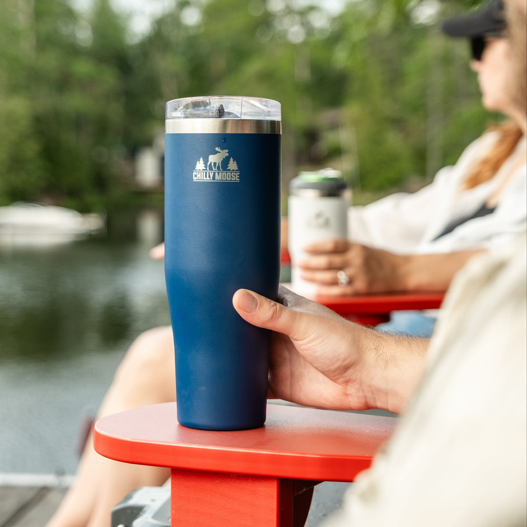 Person holding a navy blue insulated tumbler by a lake with trees in the background